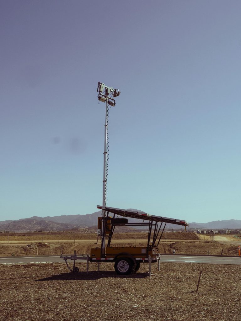 A portable light tower powered by solar panels stands in a desert landscape, showcasing renewable energy technology.